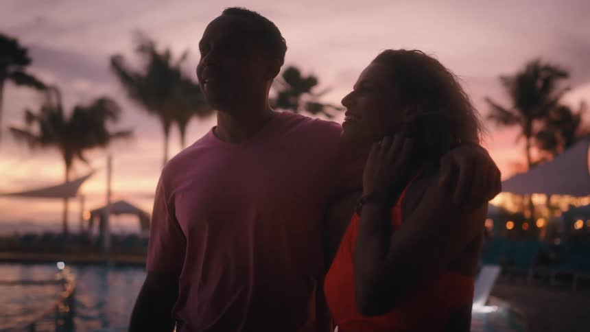 Black man and white woman stroll along on the promenade at dusk