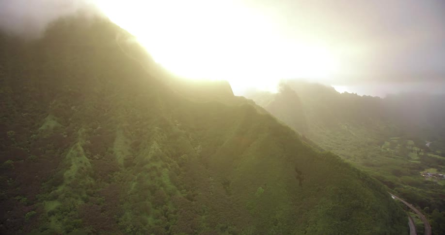 Sun glows in the mist and clouds as it rises from behind forest covered mountain