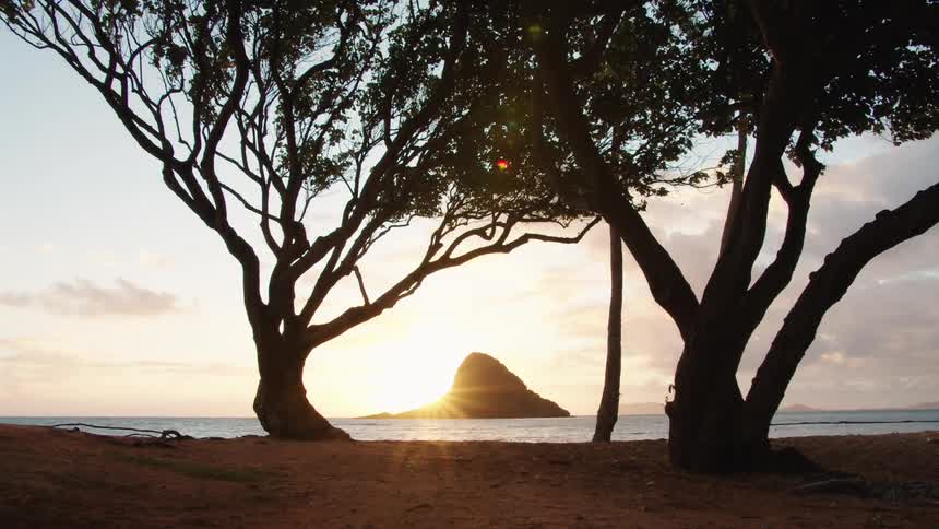 The sun rises behind an island on the ocean