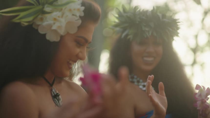 Polynesian women with flowers in their hair smile and talk as they work with flowers outdoors