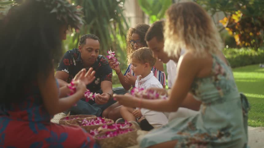 A man a woman and children sitting down making leis