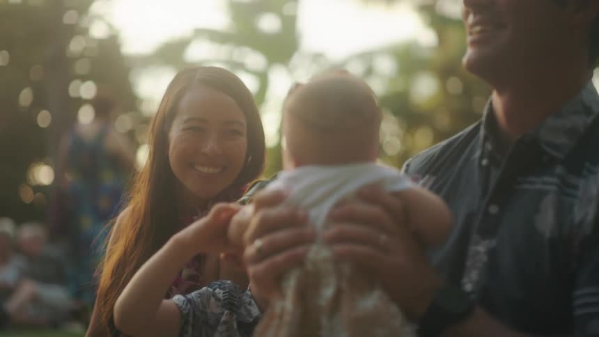 A man bounces an infant on his lap while outside with his family