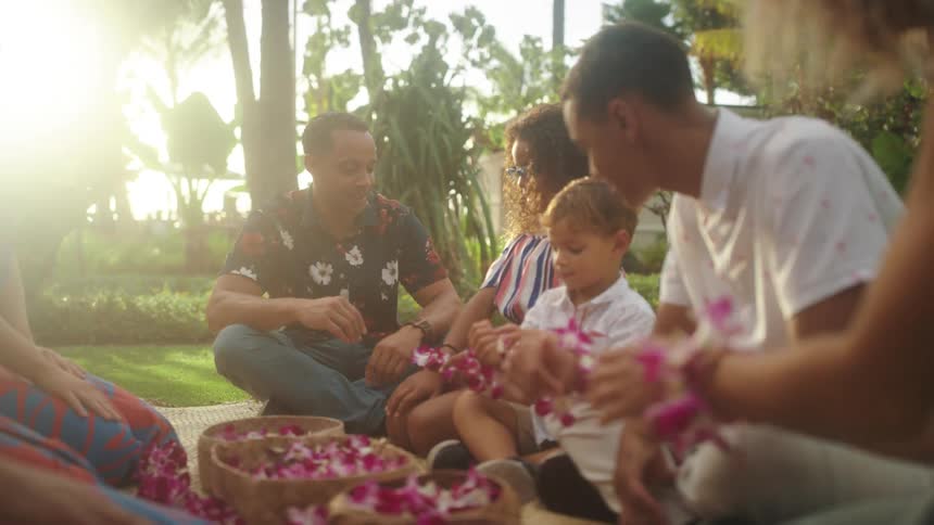 A family sitting in grass outdoors making bracelets out of flowers