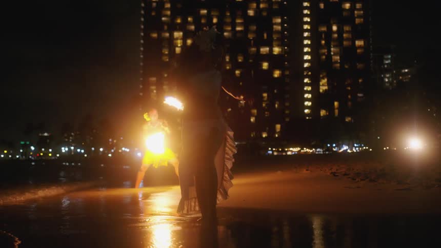 Two fire dancers are performing on the beach