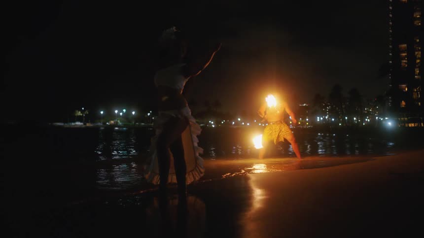 A woman dances as a man spins fire around
