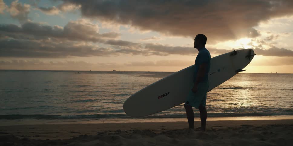 A man holds a surfboard and stands next to the ocean