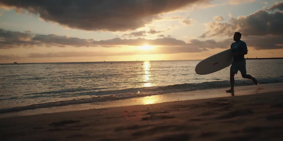 A man running on the beach holding a surfboard