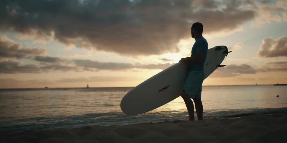 A surfer is watching the sunrise on the beach
