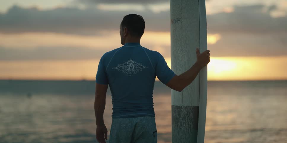 A man holding his surfboard looks out at the water