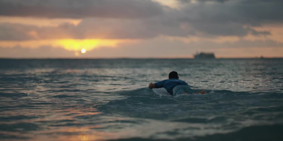 A man carrying a surfboard runs into the ocean during sunrise
