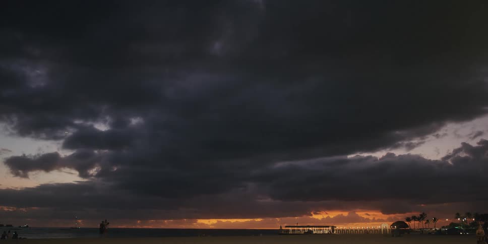 Dark clouds cover the sky while people linger near the beach