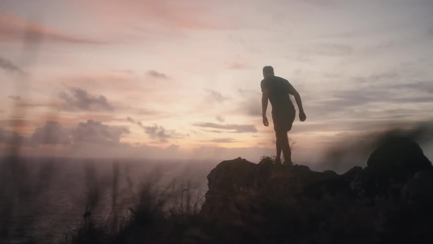 Man hikes to rock overlooking ocean at sunset