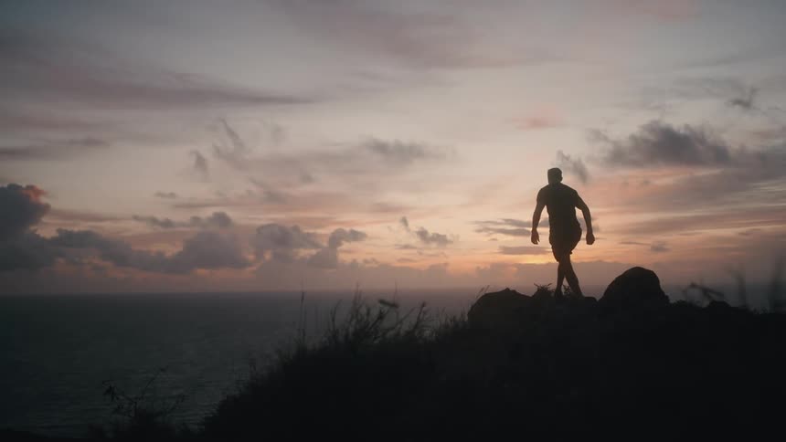 A man runs to the edge of a cliff and looks out a the water