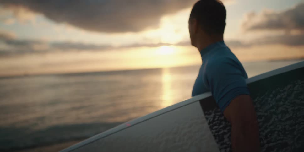 Male surfer picking up surfboard then checking out ocean at sunrise