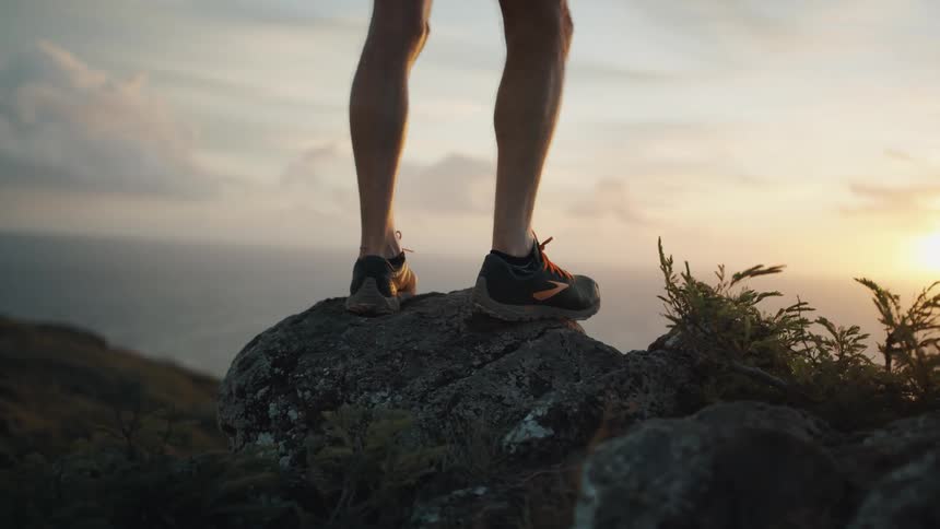 A man stands on a rock at the top of a hill