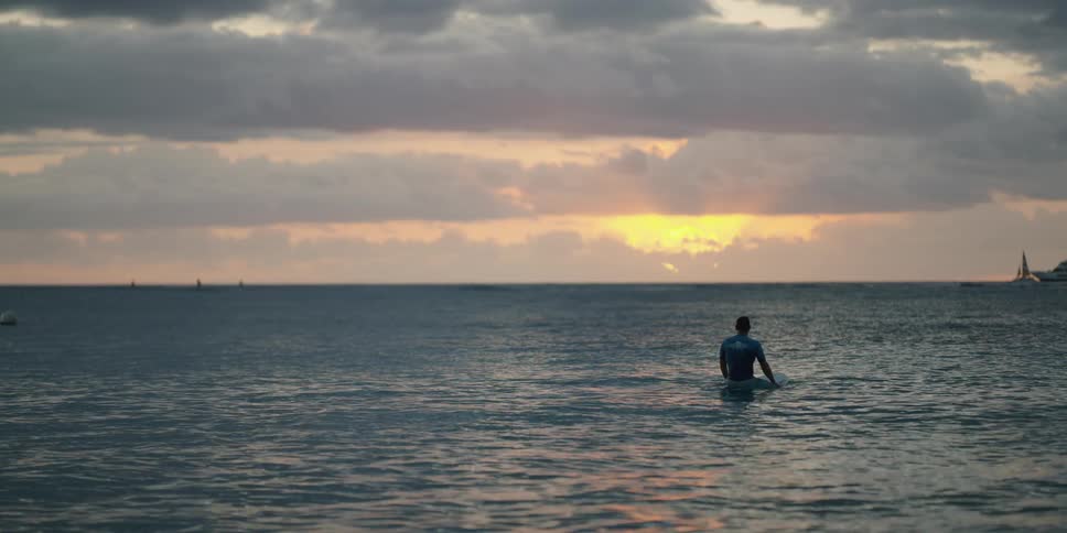 A man sitting on a surfboard in the ocean with the sky and clouds in the background