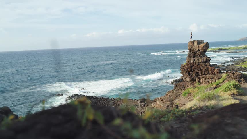 A man stands on a cliff and looks down at the water below
