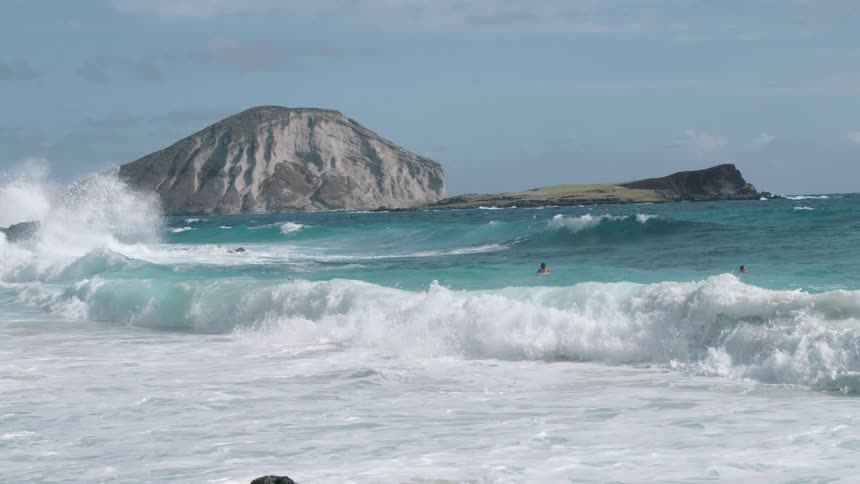 Strong waves crashing at shoreline while surfers try to surf