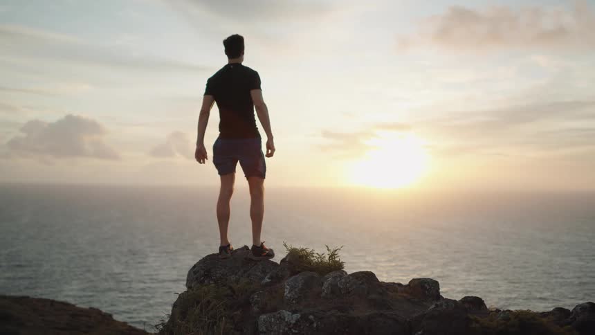 Man runs up hill to stand on promontory watching sun rise on the horizon over the ocean