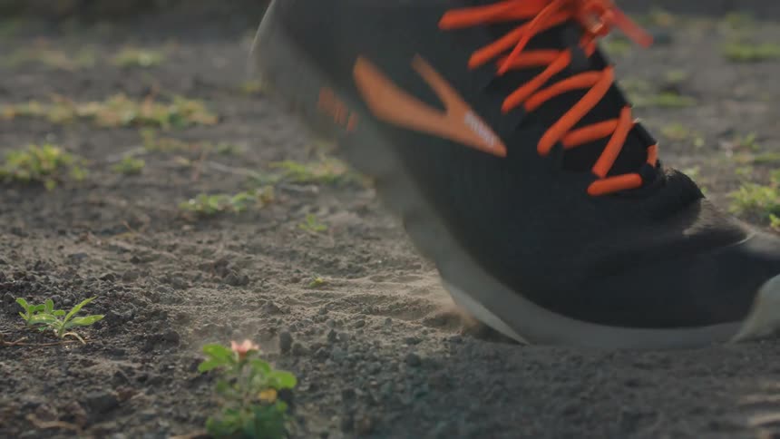A joggers sneakered foot steps in dirt and kicks it up as he runs