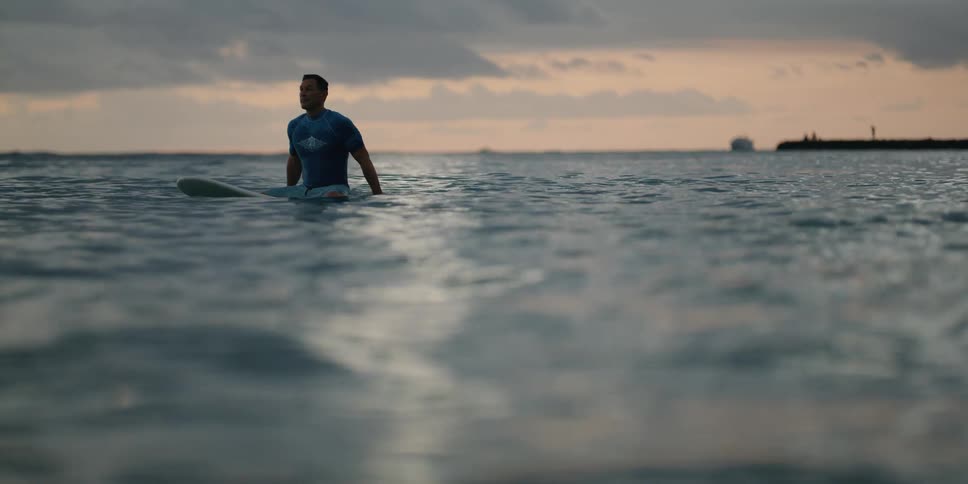 Male surfer sitting on surfboard waiting for wave at sunrise