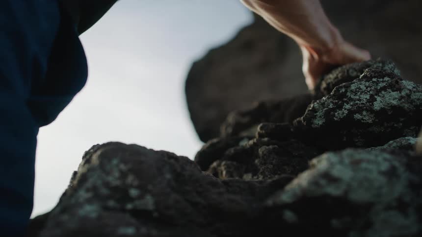A man raises his hands and grabs ahold of the mountain rock to climb up