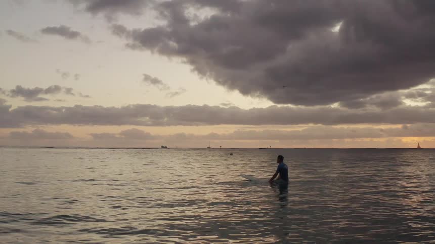 Surfer floating on surfboard in calm sea at sunset