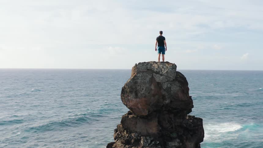 Man stands on top of tall rocks overlooking ocean