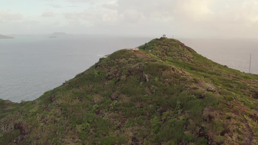 People stand on top of a hill overlooking the ocean and rocks below