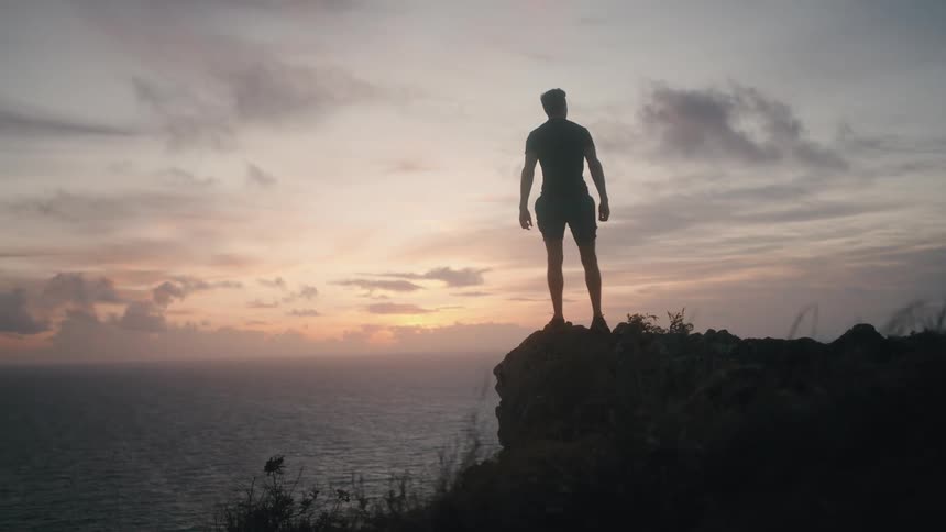 A man jogs on a mountain and raises his arms in victory when he reaches the top