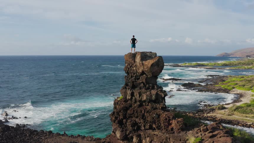 A man stands on top of a rock formation on a cliff overlooking the ocean