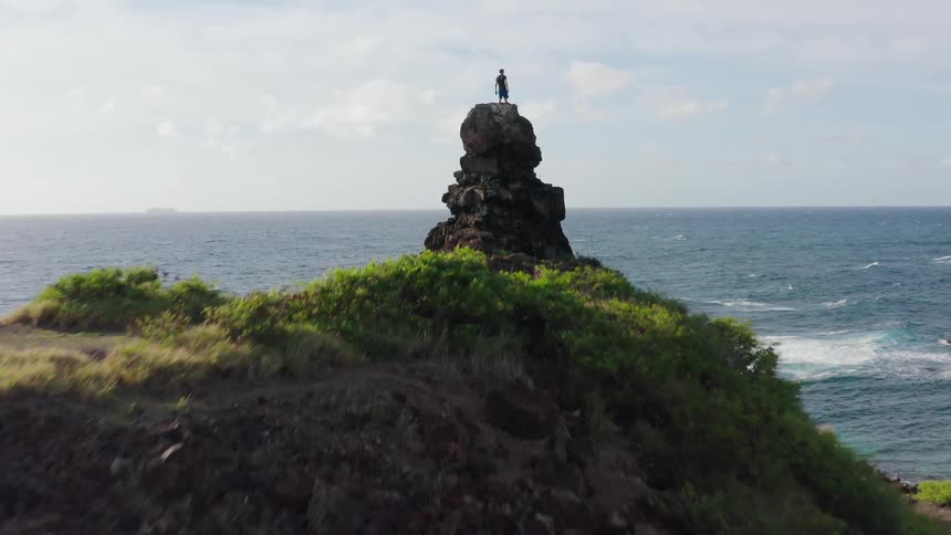 A man stands on a cliff and looks out at the water