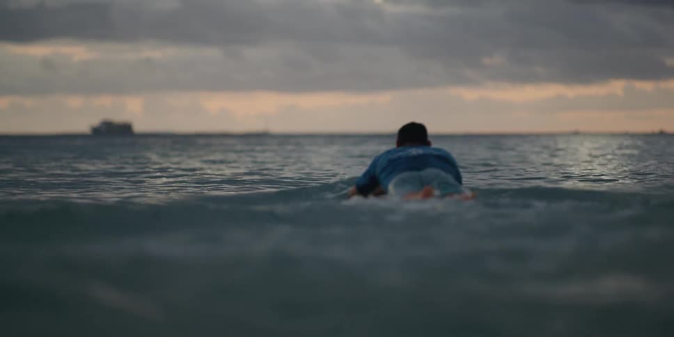 Surfer paddles surfboard out from beach toward the horizon