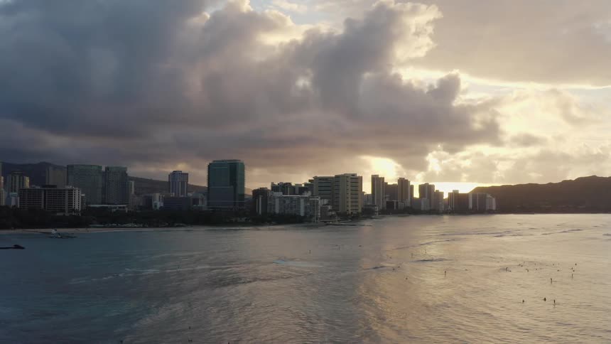 A city skyline sits under dark clouds during sunrise