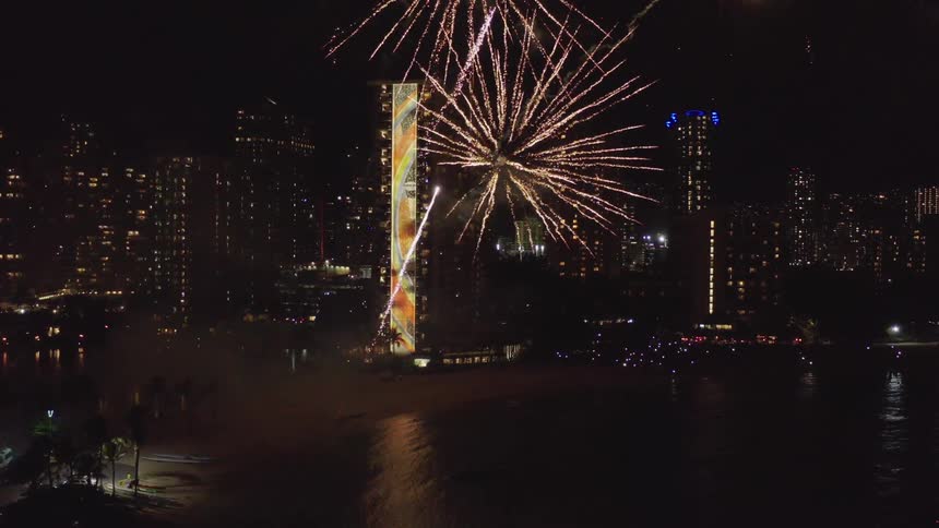 Fireworks launch from beach lighting up the sky over the city downtown at night