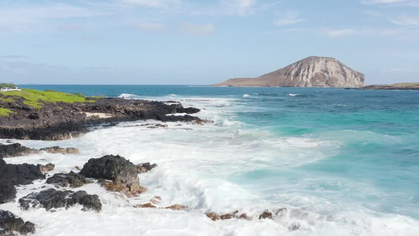 Waves crashing into a rocky shore with an island and the sky in the background
