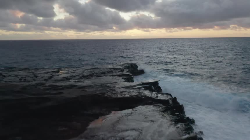 Sun peeks from behind clouds as waves crash against rocky shore