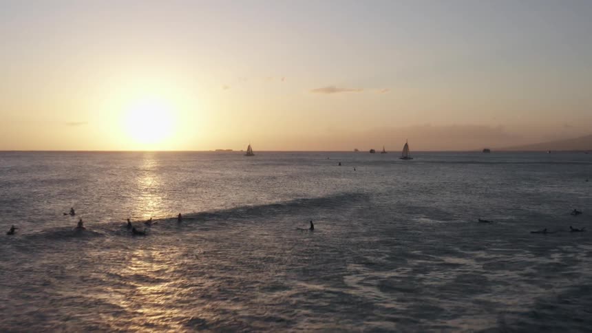 Sailboats and surfers floating on the sea at sunset
