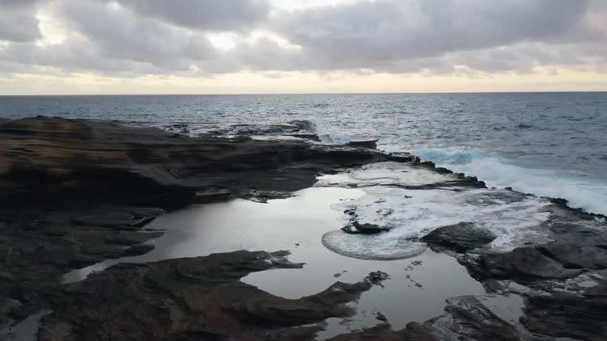 Ocean waves crash against rocks on a cloudy day