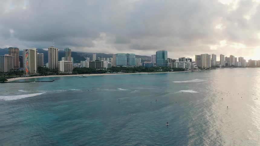 Surfers surfing in front of beachfront city at sunrise on cloudy day
