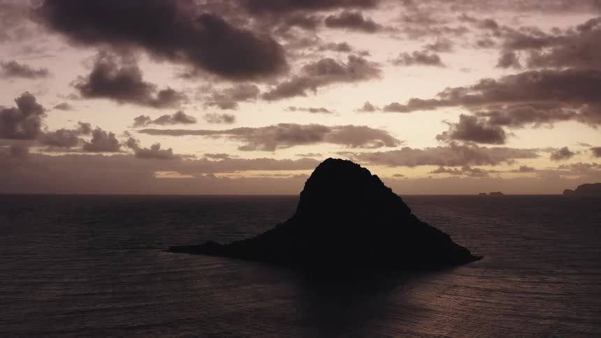Aerial of large rock formation in the ocean under cloudy skies at sunrise
