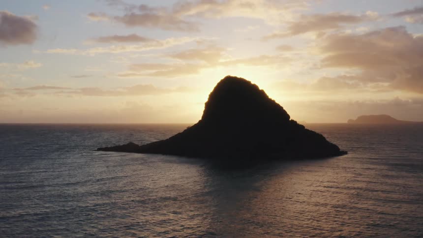 The sun sets behind a small island in the ocean