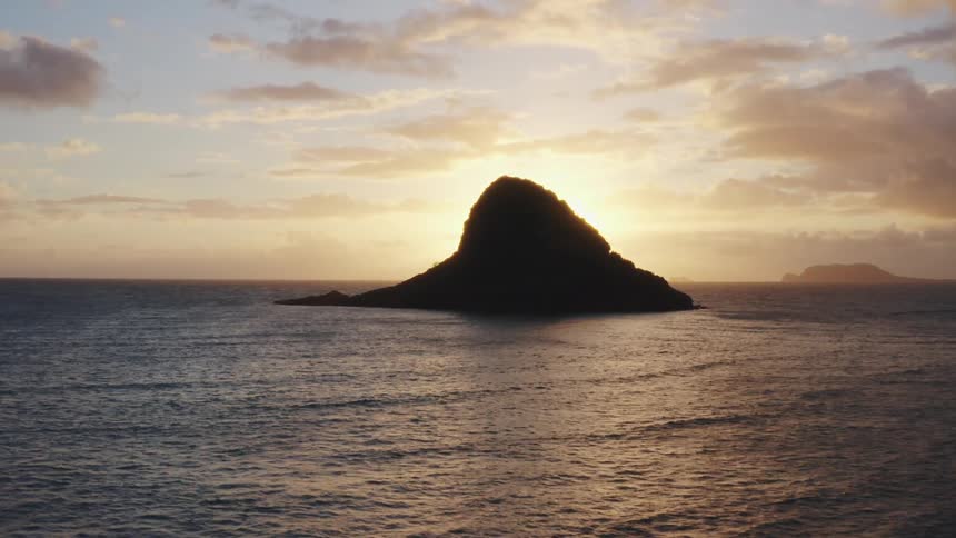 The sun sits behind a landmass jutting out of the ocean