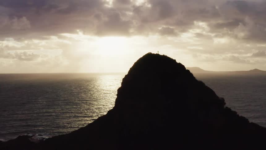 Man stands on top of island looking at sunset over the sea