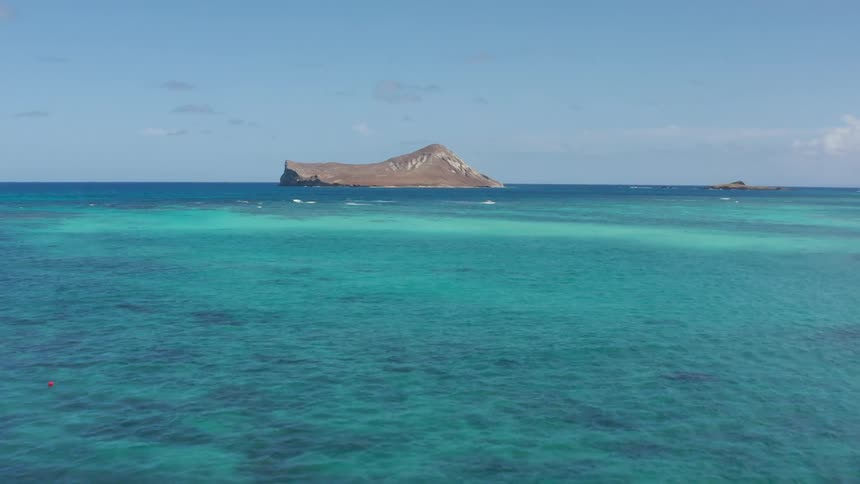 A stone island in a light blue ocean during the day