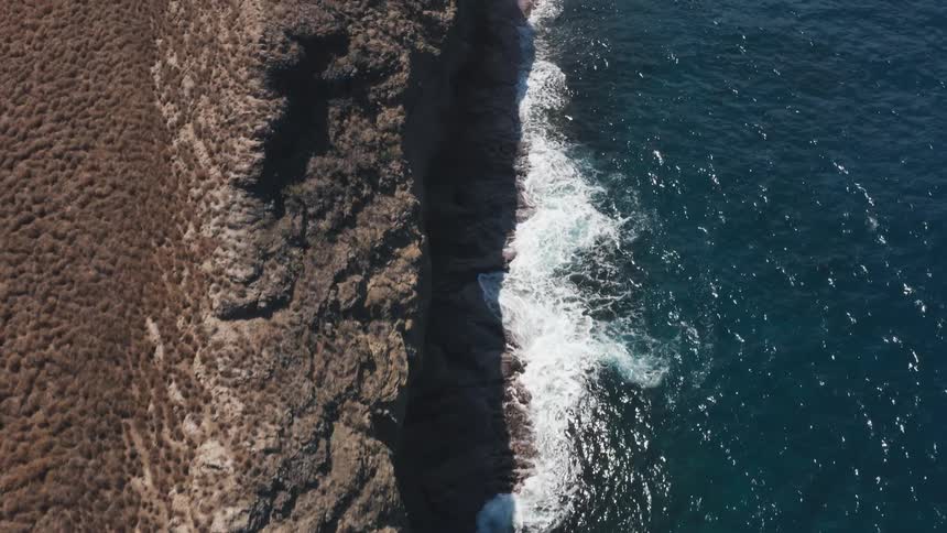 Aerial view of ocean waves crashing against rocks on a sunny day