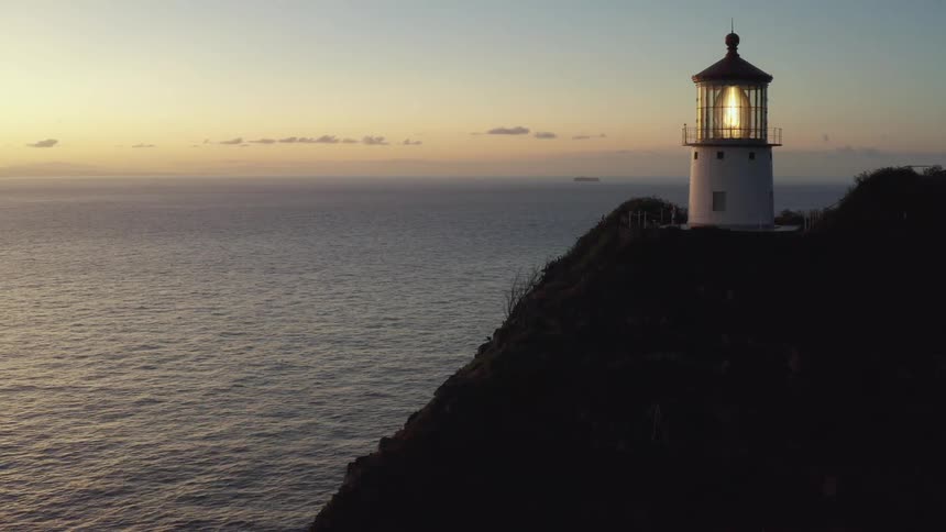 Beacon in lighthouse standing on promontory blinks as the sky lightens