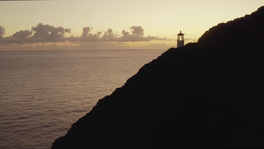 Lighthouse on cliffside above ocean at dawn