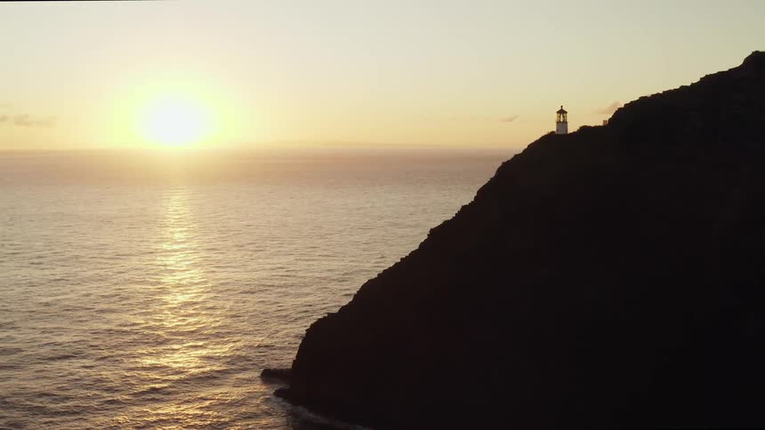 Lighthouse stands on promontory as sun rises over the ocean