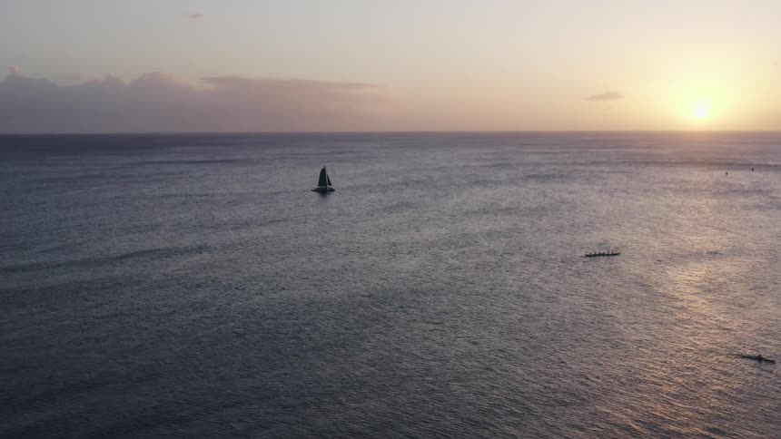A sail boat on the calm ocean under a low sun